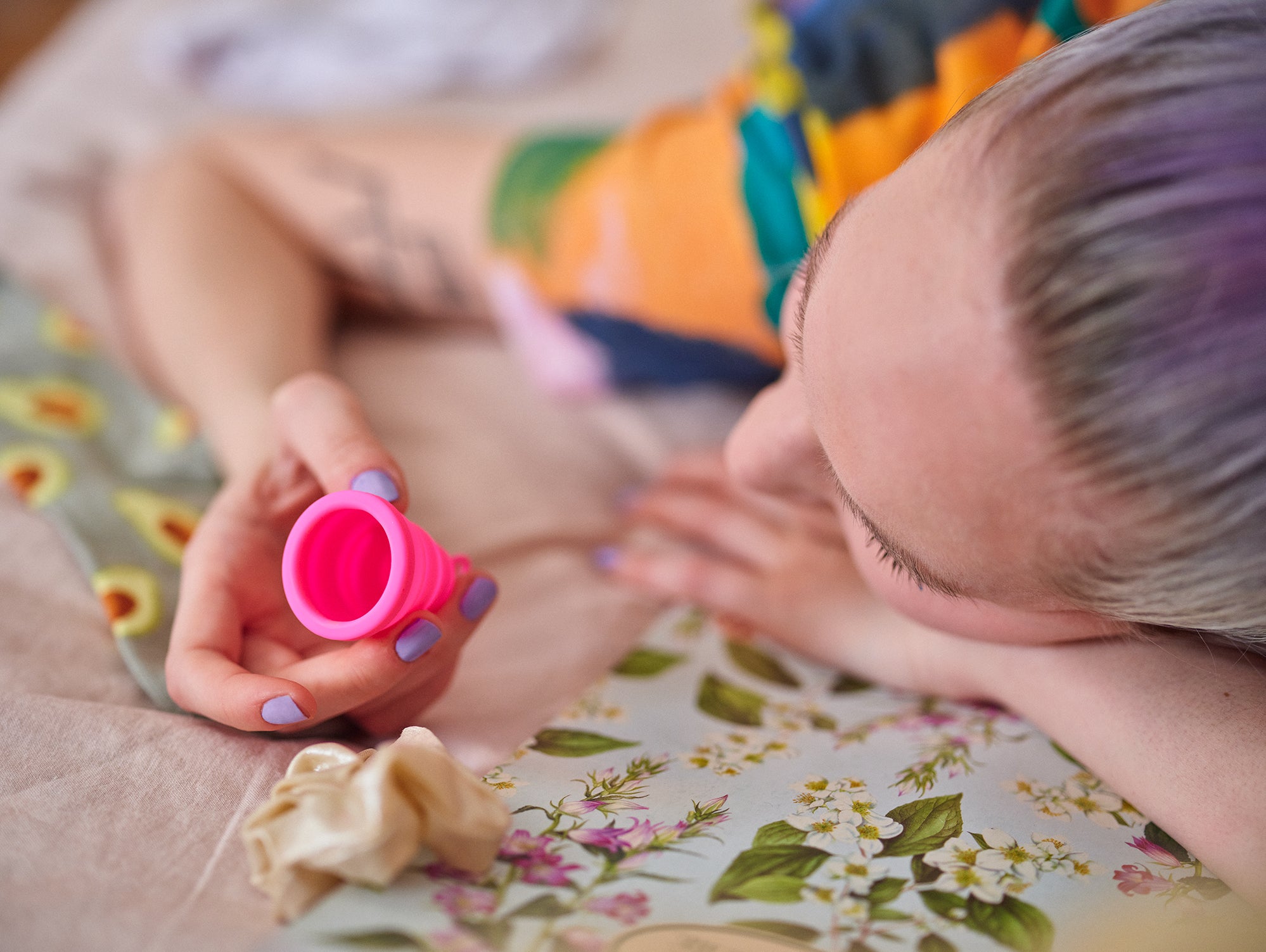 a women on a colourful bed with a pink menstrual cup Our classic Itimina lily one period cup . This menstrual cup is made from reusable soft silicone, the perfect eco-choice for sister's who want a safe, healthy, non toxic, latex free, BPA free and waste free period product.provides 8 hours of protection. הגביעונית הכי טובה ונוחה בישראל, תהני מכוס מחזור שלך