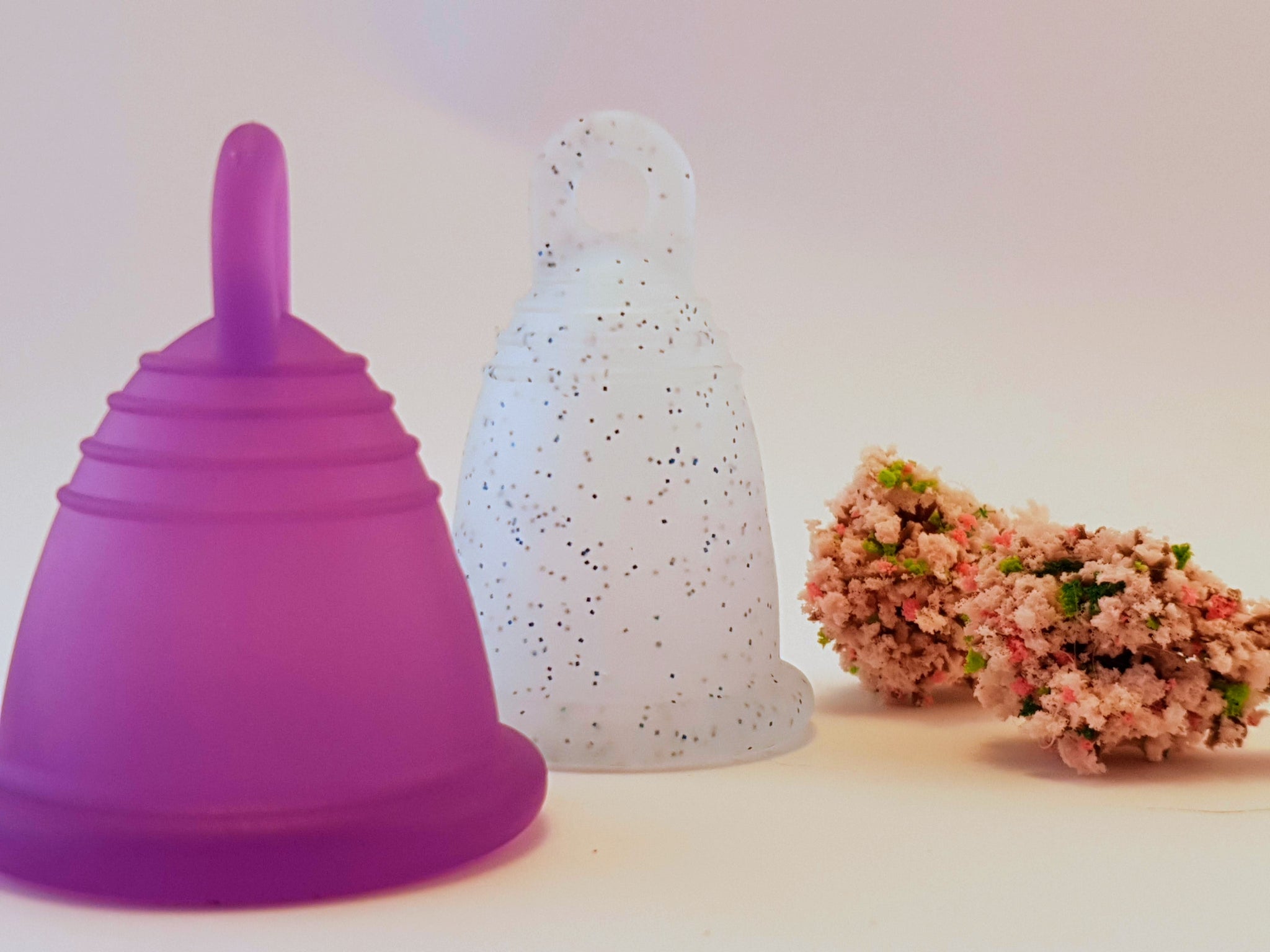 blue glitter menstrual cup, white background and pink flowers and a purple menstrual cup, classic Meluna . This menstrual cup is made from reusable soft silicone, the perfect eco-choice for sister's who want a safe, healthy, non toxic, latex free, BPA free and waste free period product lifestyle. Easy to use and provides 12 hours of protection. גביעונית מחזור או כוס לווסת הכי טובה ונוחה בארץ